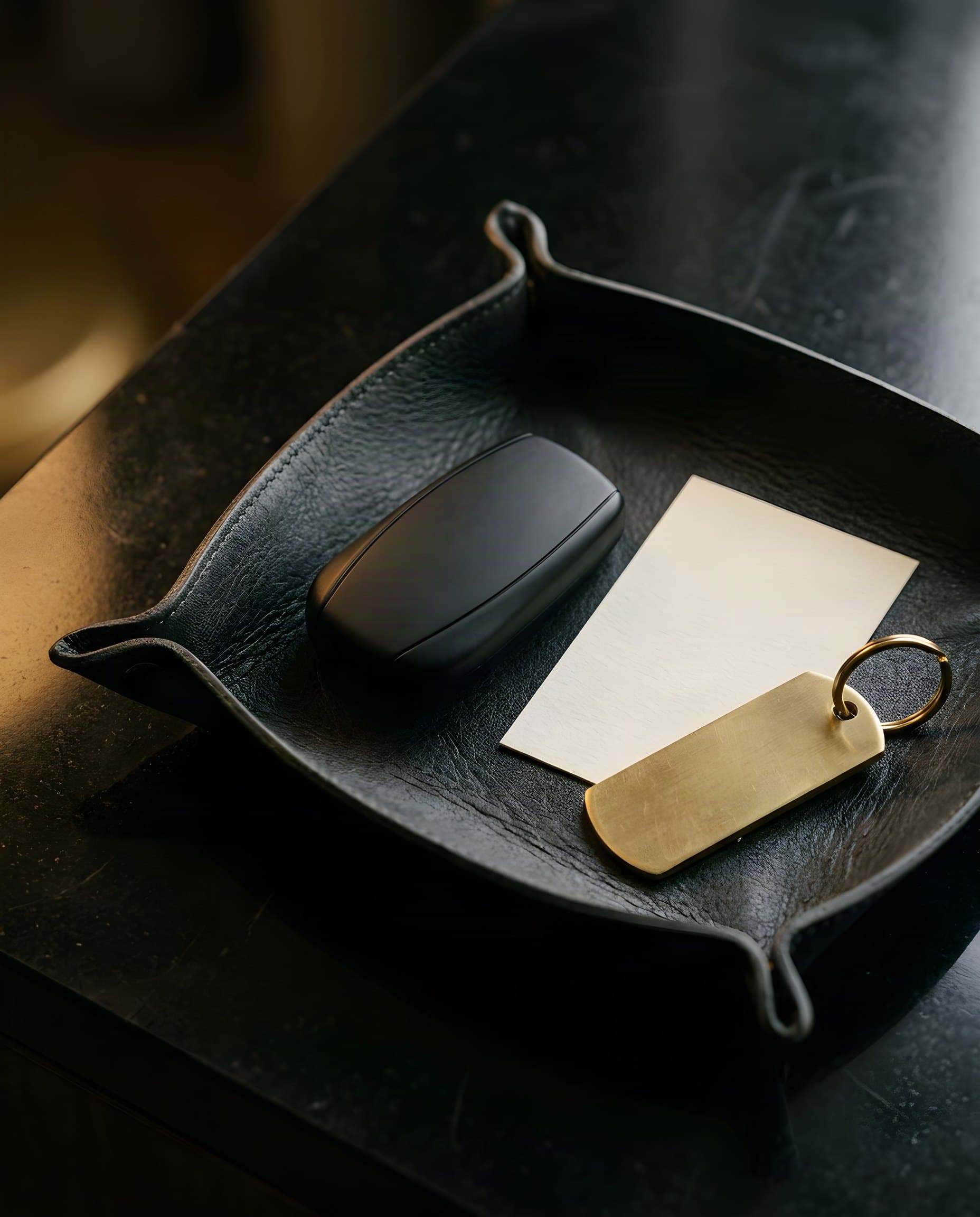 Leather tray with a car key, brass key tag and a blank card on dark stone